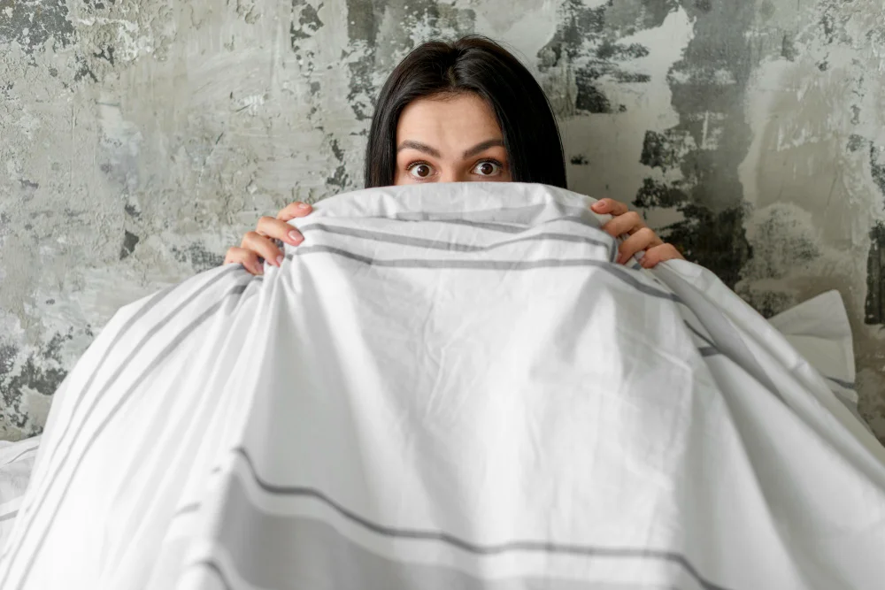 Mujer con tapando la cara con cobija, con temor de ver algo